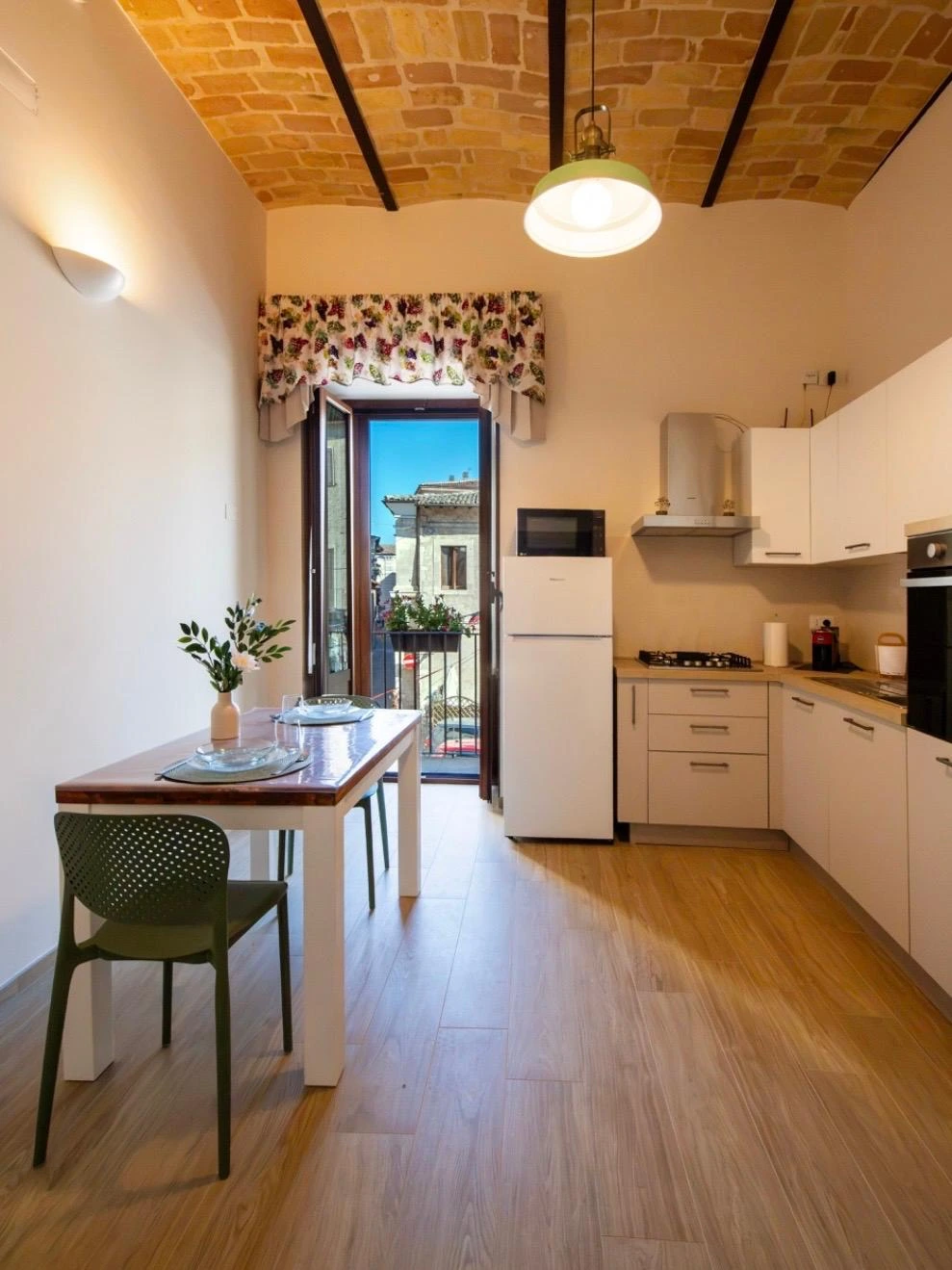 La cucina della Dimora in piena luce del giorno, con il balcone aperto sul centro storico